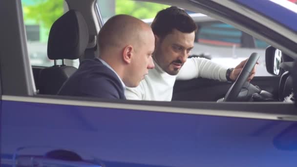 Vendedor profissional sorrindo mostrando um carro novo na concessionária para seu cliente masculino — Vídeo de Stock