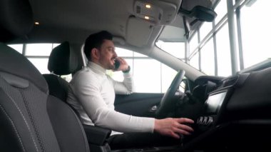 İş adamı araba galerisinde telefonla konuşuyor. Yeni bir arabada oturuyor. Araba satışı konsepti