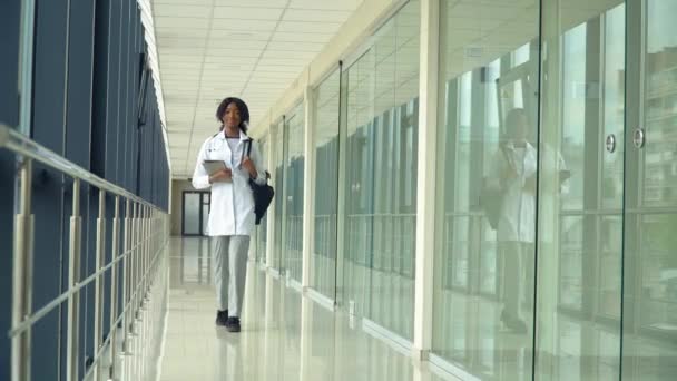 Estudiante interno afroamericano caminando en el hospital con una tableta. Nueva instalación médica moderna totalmente funcional. Concepto de medicina, salud y personas — Vídeo de stock