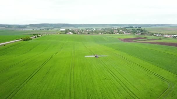 Luchtfoto van landbouwtrekkers die op het veld sproeien met sproeiapparaten, herbiciden en pesticiden. Tractor spuit pesticiden op graanveld — Stockvideo