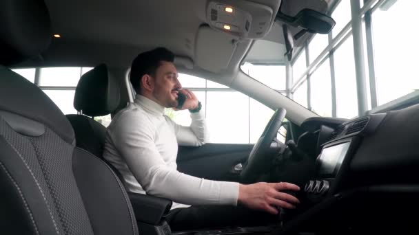 El hombre de negocios está hablando por teléfono en la sala de exposición del coche sentado en un coche nuevo. Concepto de venta de coches — Vídeo de stock