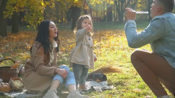 Familie bläst Luftblasen. Mutter und Vater mit Tochter amüsieren sich im Freien. Picknick im Herbstpark — Stockvideo