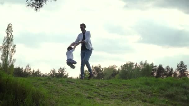 日落时,爸爸把一个孩子的手扭在公园上.爸爸和儿子周末在公园里玩耍。快乐的童年父亲节快乐 — 图库视频影像