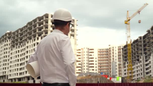 Construtor masculino arquiteto engenheiro em chapéu duro leitura de planta no canteiro de obras. Conceito de construção — Vídeo de Stock