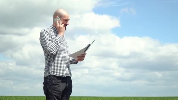 The farmer is talking on the phone on the wheat field. Agronomist or farmer examines the growth of wheat — Stock Video