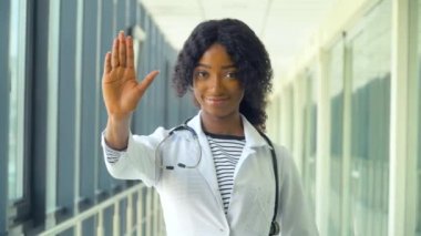 Modern bir hastanenin koridorundaki işinden memnun gülümseyen Afrikalı Amerikalı kadın doktor portresi. Koronavirüsü durdurun. Salgının sonu