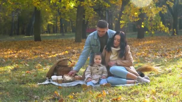 Madre y padre con hija divirtiéndose al aire libre. Picnic en el parque de otoño — Vídeo de stock