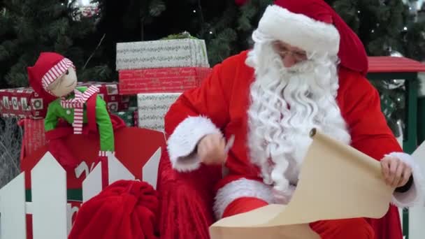 Bad Santa Claus se sienta con una bolsa de regalos y se sopla la nariz en el centro comercial — Vídeo de stock