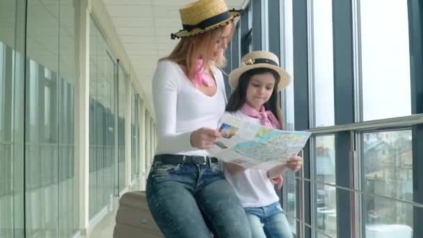 Krásná žena s holčičkou drží turistickou mapu na letišti a vybírá si, kam v novém městě — Stock video