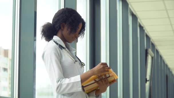 Afroamerikansk student praktikant med en bok på sjukhuset. Ny modern fullt fungerande medicinsk anläggning. Begreppet medicin, hälsovård och människor, utbildning på nätet — Stockvideo
