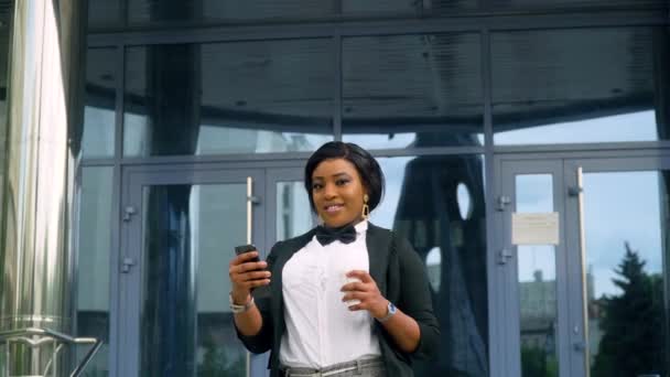 Αφροαμερικάνα νέα επιχειρηματίας με κοστούμι και λευκό πουκάμισο με τηλέφωνο και καφέ κοιτάζοντας την κάμερα έξω κοντά στο σύγχρονο κτίριο γραφείων. Λήξη καραντίνας — Αρχείο Βίντεο