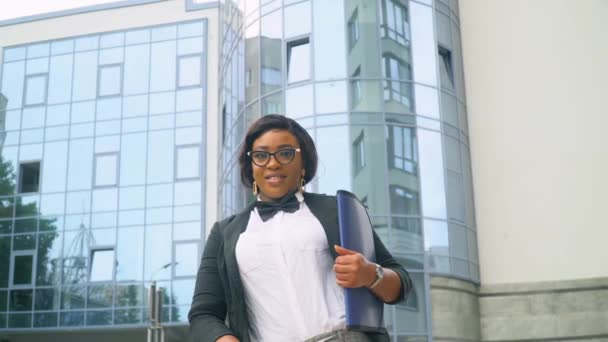 Mujer de negocios joven afroamericana en traje y camisa blanca con documentos mirando a la cámara exterior cerca del moderno edificio de oficinas. Fin de la cuarentena — Vídeo de stock