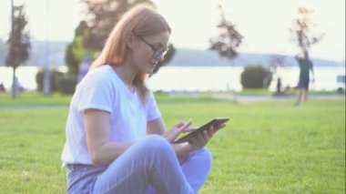Parkta tablet üzerinde serbest çalışan genç bir kadın. uzak çalışma