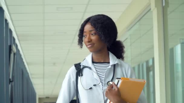 Afro-Amerikaanse student stagiaire met een boek in het ziekenhuis. Nieuwe moderne volledig functionele medische faciliteit. Begrip geneeskunde, gezondheidszorg en mensen, online onderwijs — Stockvideo