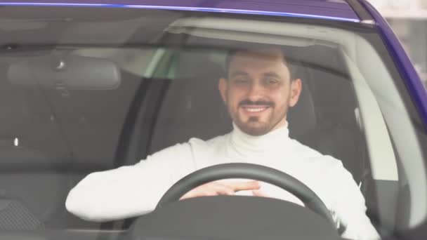 Muž se usmívá a tančí v novém autě v prodejně aut. Veselý muž se raduje z koupě nového auta — Stock video