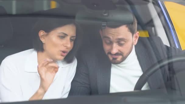 Homem elegante sentado no salão de beleza do carro e conversando com negociante de carro feminino. Profissional ajudando o cliente a escolher o melhor automóvel no showroom — Vídeo de Stock