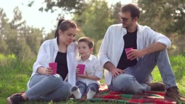 Anne, baba ve oğul parkta bir piknikte meyve suyu içerler. Ortak bir aile sağlıklı bir yaşam tarzı ister. Mutluluk kavramı
