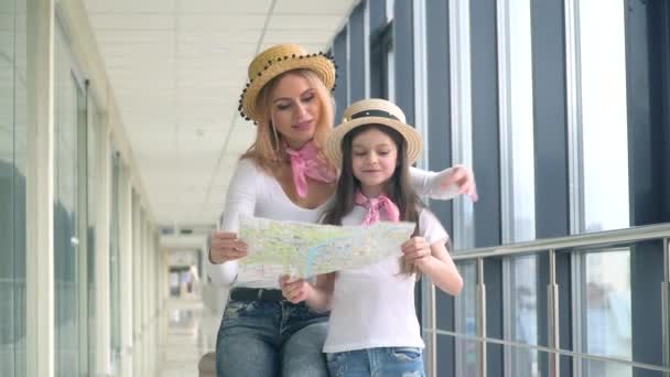 Mooie vrouw met klein meisje met een toeristische kaart op de luchthaven — Stockvideo