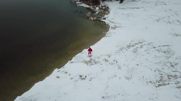 Der Weihnachtsmann steht mit einer Geschenktüte am verschneiten Ufer des Sees. Weihnachtsmann in der Arktis. Ansicht von oben — Stockvideo