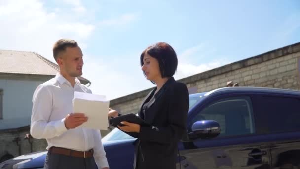 Pareja de negocios con documentos y tableta cerca del coche al aire libre. Concepto de personas y negocios — Vídeos de Stock