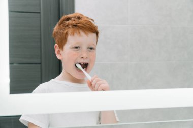 Çocuk sabah banyoda aynanın önünde dişlerini fırçalıyor.