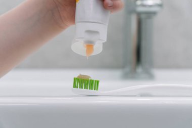 Banyoda dişlerini fırçalayan bir çocuk. Küçük çocuk diş macununu fırçaya koyar.