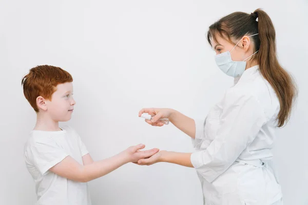 En kvinnlig läkare desinficerar små pojkars händer med en antiseptisk spray. Skydd av Covid-19. Stoppa coronavirus — Stockfoto