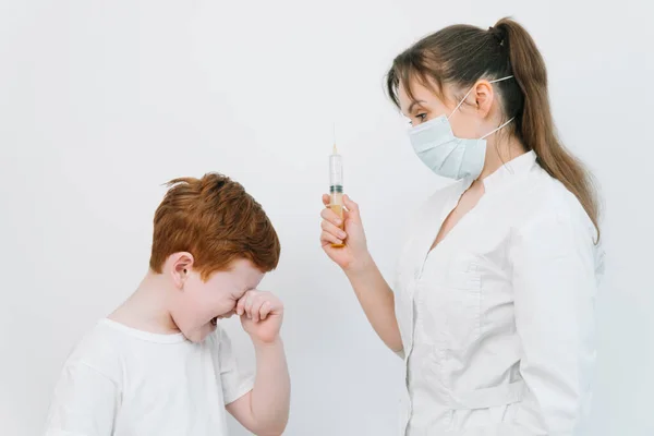 Kleine jongen is bang voor de dokter met een spuit. Baby huilt bang injectie. De dokter geeft het kind een griepprik. — Stockfoto