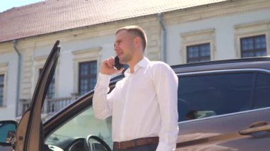 İş adamı, arabanın yanında telefonla konuşuyor. Teknoloji ve araba konsepti