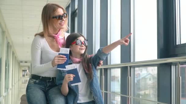 Жінка і маленька дівчинка, що має паспорти та квитки на посадку авіакомпанії. Посадковий талон та паспорт в аеропорту. Дівчина показує на літаку, що прибуває — стокове відео