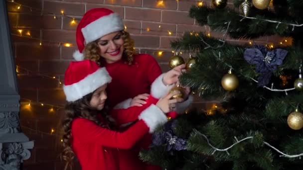 Moeder en dochter in kerstkostuums versieren de kerstboom met decoraties en speelgoed — Stockvideo