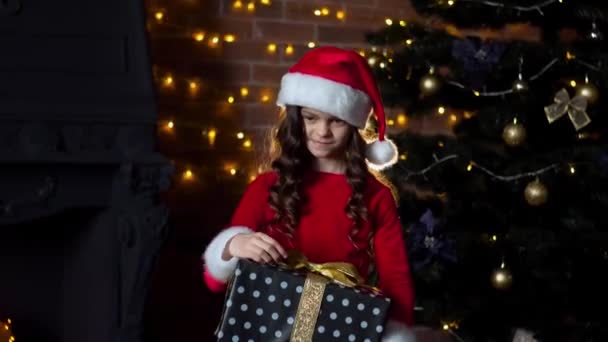 Кудрявая девушка в рождественском костюме держит подарок возле елки — стоковое видео