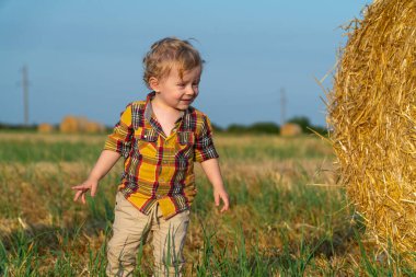 Küçük sarı saçlı çocuk buğday tarlasında balyalarla oynuyor.