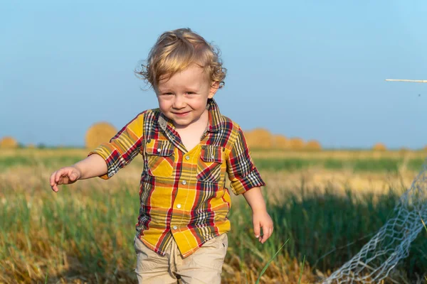 Küçük sarı saçlı çocuk buğday tarlasında balyalarla oynuyor.