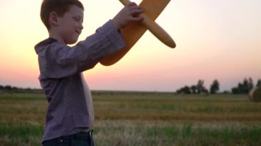 Kızıl saçlı çocuk balyalarla buğday tarlasında oyuncak bir uçakla oynuyor. Yavaş çekim
