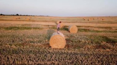 Kızıl saçlı çocuk balyalarla buğday tarlasında oyuncak bir uçakla oynuyor.