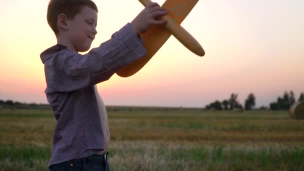 Il ragazzo dai capelli rossi gioca con un aeroplano giocattolo su un campo di grano con balle. Rallentatore — Video Stock