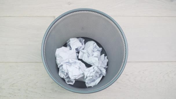 Throw crumpled into the trash. Overflowing waste paper in office garbage bin. Junk, wastepaper in rubbish isolated on wooden background — Stock Video
