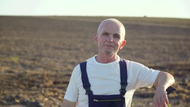 A senior farmer standing through a field with rake — Stock Video