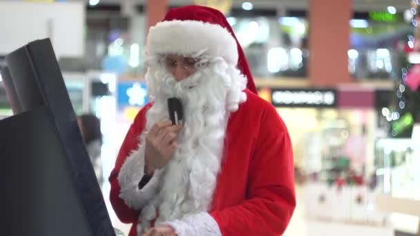 Büyük bir alışveriş merkezinde bankomatın yanında kredi kartı olan Noel Baba. — Stok video