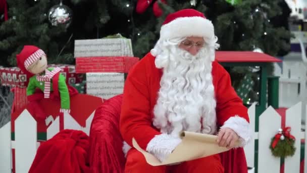 Santa Claus sits with a bag of presents on the emporium writes something to the list — Stock Video