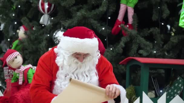 Böser Weihnachtsmann zerreißt Geschenkliste. Der Weihnachtsmann sitzt mit einem Sack voller Geschenke im Einkaufszentrum und schreibt etwas auf die Liste — Stockvideo