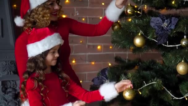 Мама і дочка у різдвяних костюмах прикрашають ялинку прикрасами і іграшками. — стокове відео