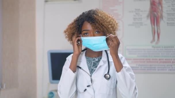 Afroamerikanische Ärztin setzt im Krankenhaus medizinische Maske auf, im Hintergrund Ultraschallgeräte. Virus stoppen — Stockvideo