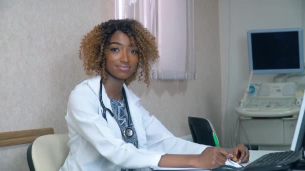 Estudante afro-americano estagiário no hospital com aparelhos de ultra-som em segundo plano. Nova moderna instalação médica totalmente funcional. Conceito de medicina, cuidados de saúde e pessoas, educação online — Vídeo de Stock