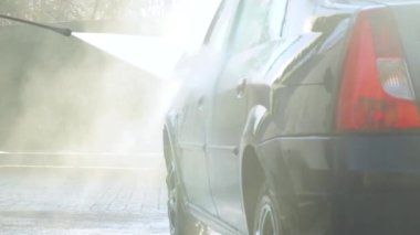 Bir adam makineyi yüksek basınçlı ekipmanla yıkar. Yüksek basınçlı bir su püskürtüsü arabanın kirini temizler. Araba yıkama servisi.