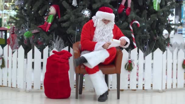 Babbo Natale si siede con una borsa di regali sul centro commerciale scrive qualcosa alla lista — Video Stock