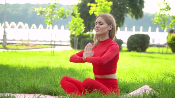 Młoda kaukaska kobieta relaksująca się ćwicząc jogę w parku nad jeziorem — Wideo stockowe