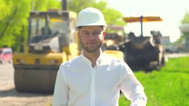 Tamirhanenin müdürünün portresi beyaz bir miğferle yol inşaatının arka planına karşı işliyor.