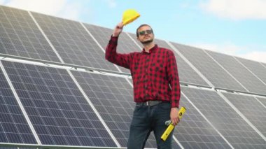 Bir mühendis güneş panellerini kontrol ediyor. Bir güneş enerjisi istasyonunun arka planında başarılı genç bir mühendisin portresi